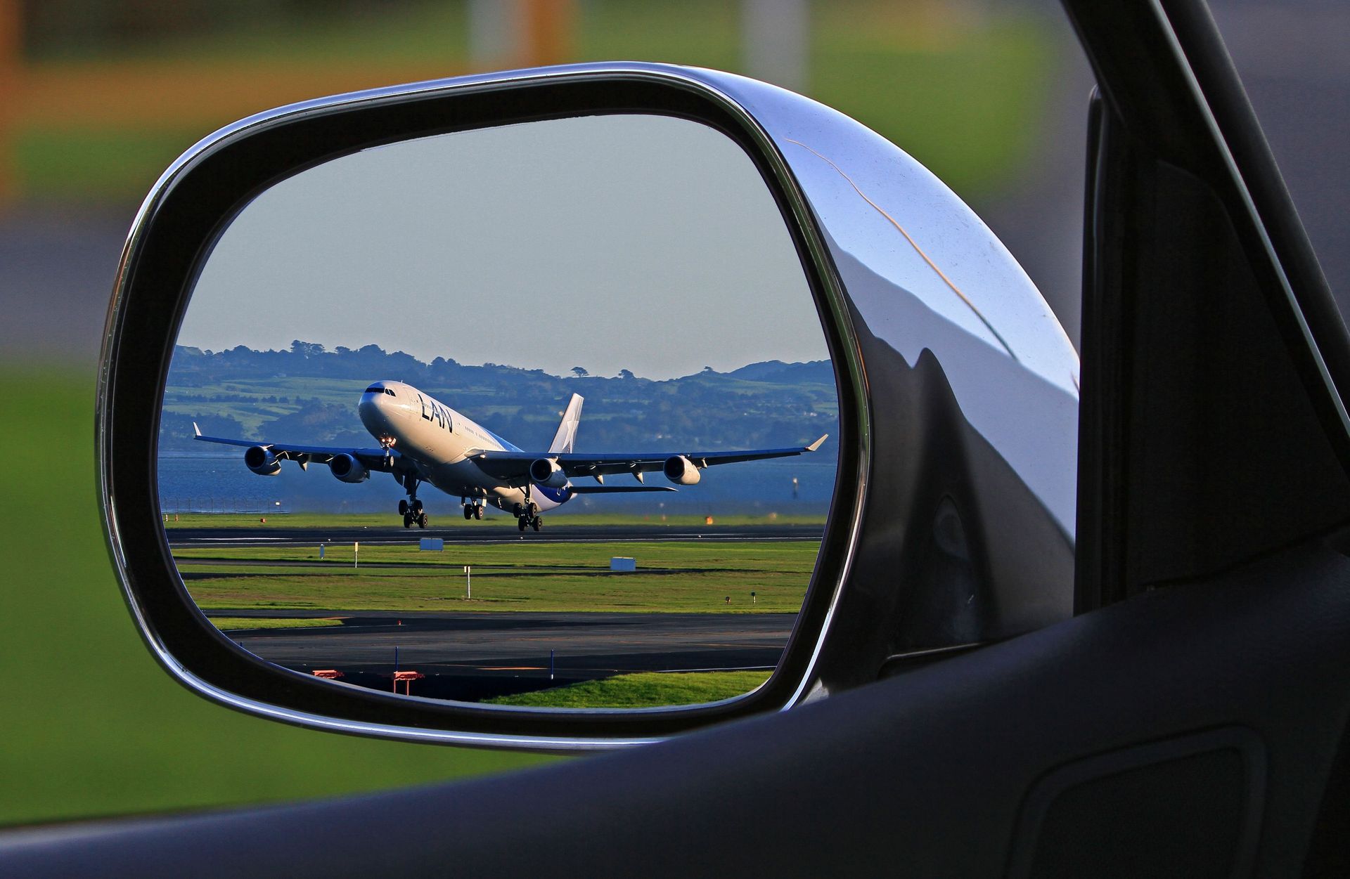 A jet airplane taking off is reflected in a car's side mirror, capturing a unique aviation perspective.